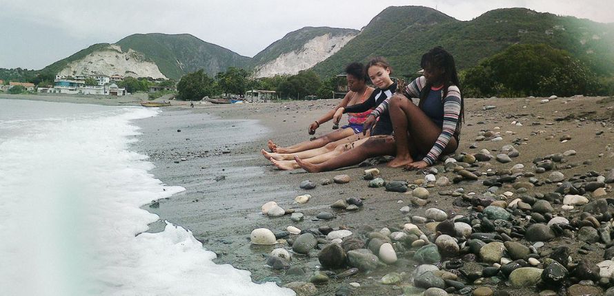 Three girls sitting on a rocky beach.